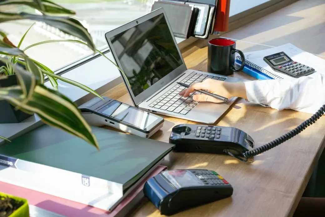 Bàn làm việc với laptop, điện thoại, máy tính, sổ sách rời rạc